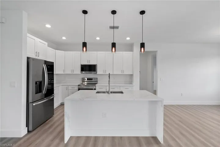 Kitchen featuring appliances with stainless steel finishes, white cabinetry, and an island with sink