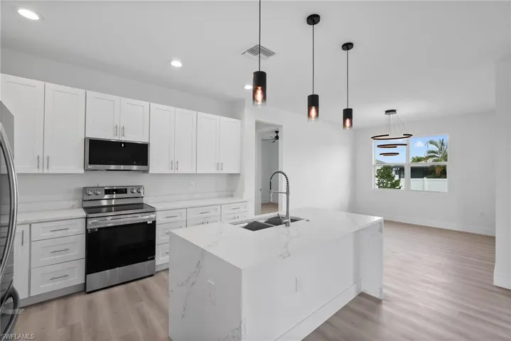 Kitchen with stainless steel appliances, white cabinets, a center island with sink, and hanging light fixtures