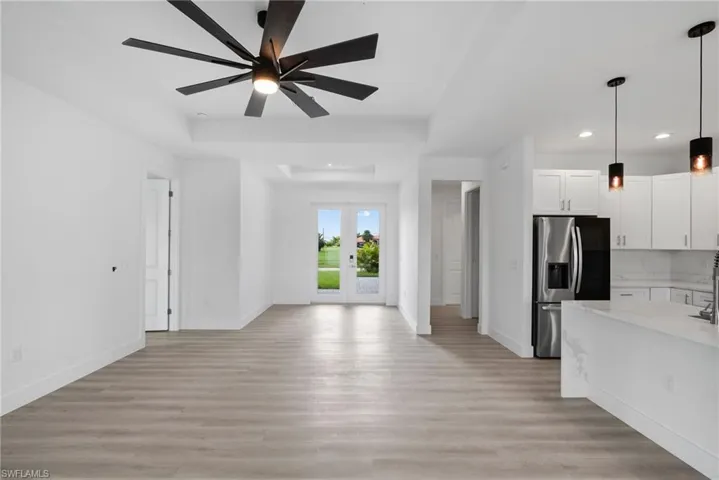 Kitchen with light wood-type flooring, light stone counters, white cabinetry, ceiling fan, and stainless steel fridge