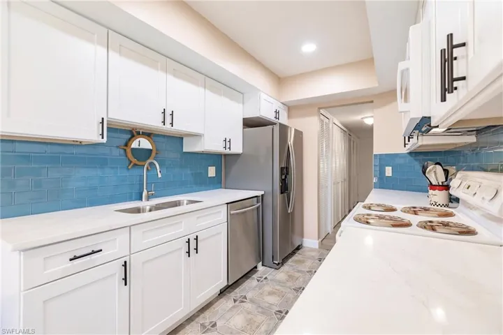 Kitchen featuring light stone counters, sink, white cabinets, and stainless steel appliances