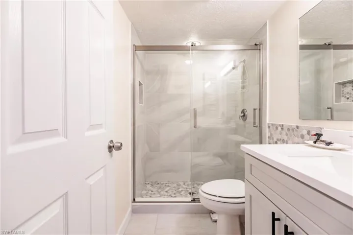 Bathroom featuring toilet, a textured ceiling, tile patterned floors, and a shower with door