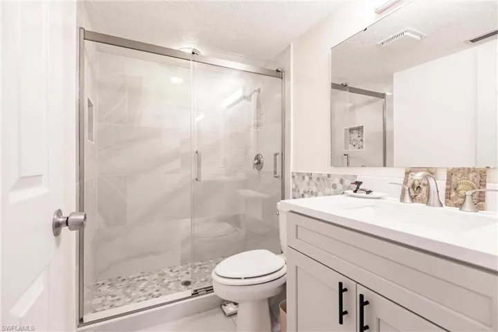 Bathroom featuring vanity, toilet, a textured ceiling, and walk in shower
