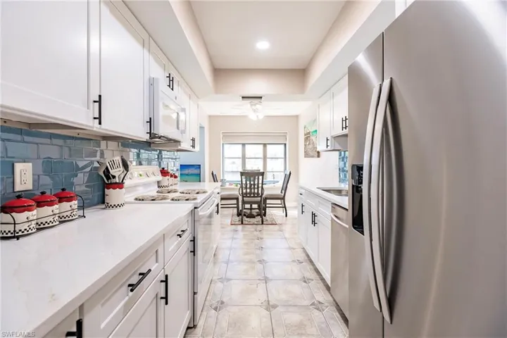 Kitchen with white cabinets, decorative backsplash, ceiling fan, light stone countertops, and appliances with stainless steel finishes