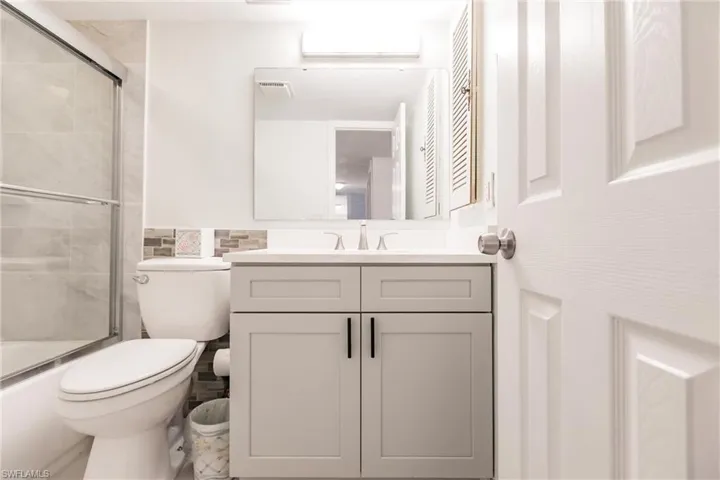 Full bathroom with a wall mounted air conditioner, vanity, toilet, and enclosed tub / shower combo