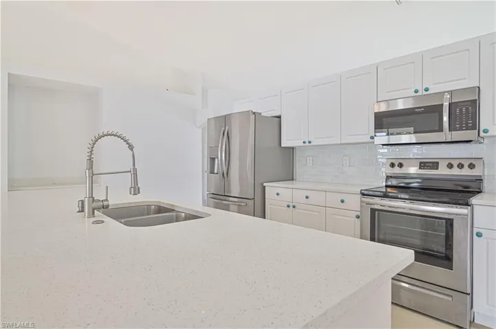 Kitchen featuring stainless steel appliances, backsplash, white cabinetry, light stone countertops, and sink