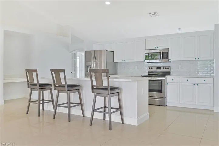 Kitchen with light tile flooring, a kitchen island, stainless steel appliances, backsplash, and a breakfast bar