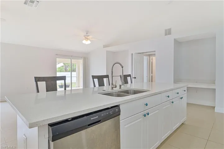 Kitchen with stainless steel dishwasher, an island with sink, sink, ceiling fan, and light tile floors