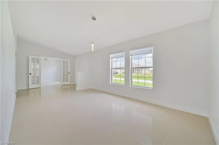 Empty room featuring vaulted ceiling, ceiling fan, light tile floors, and french doors