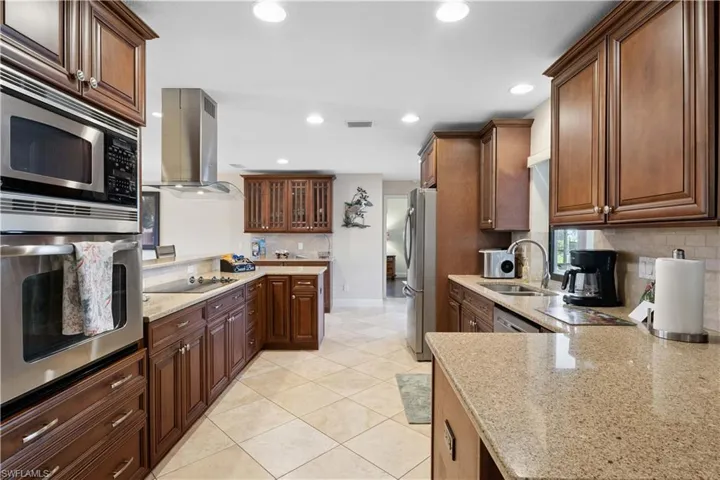 Kitchen with island range hood, stainless steel appliances, backsplash, light stone counters, and recessed lighting