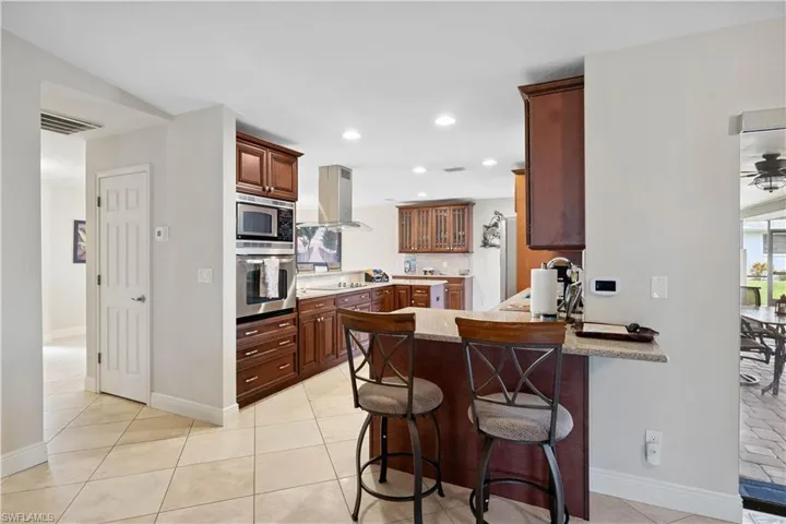 Kitchen with appliances with stainless steel finishes, island range hood, a peninsula, recessed lighting, and a breakfast bar