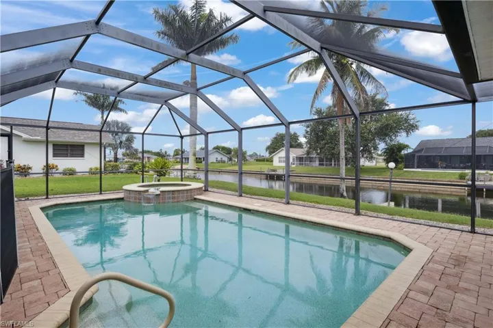View of swimming pool featuring a water view, a pool with connected hot tub, glass enclosure, and a patio