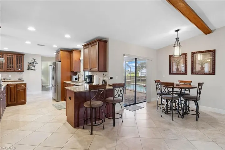 Kitchen featuring freestanding refrigerator, a breakfast bar area, light tile patterned floors, decorative backsplash, and recessed lighting