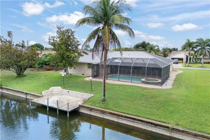 Dock with a water view, a yard, glass enclosure, and a pool with connected hot tub