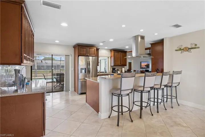 Kitchen with island exhaust hood, stainless steel fridge, a peninsula, light stone countertops, and a breakfast bar area