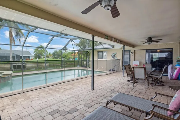 View of pool featuring ceiling fan, a patio area, glass enclosure, a pool with connected hot tub, and a water view