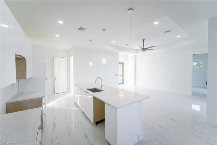 Kitchen featuring white cabinetry, sink, a tray ceiling, and an island with sink