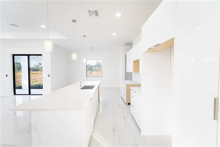 Kitchen with sink, a kitchen island with sink, hanging light fixtures, and white cabinets