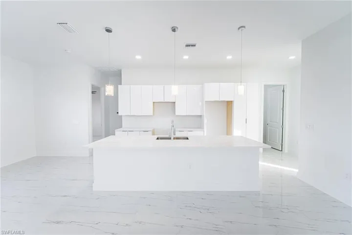 Kitchen featuring hanging light fixtures, white cabinetry, a kitchen island with sink, and sink