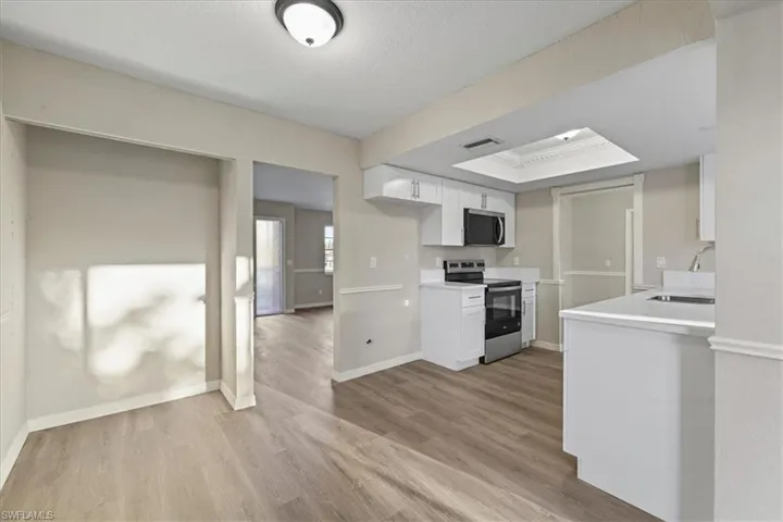 Kitchen featuring light countertops, stainless steel appliances, white cabinets, light wood-style floors, and a raised ceiling