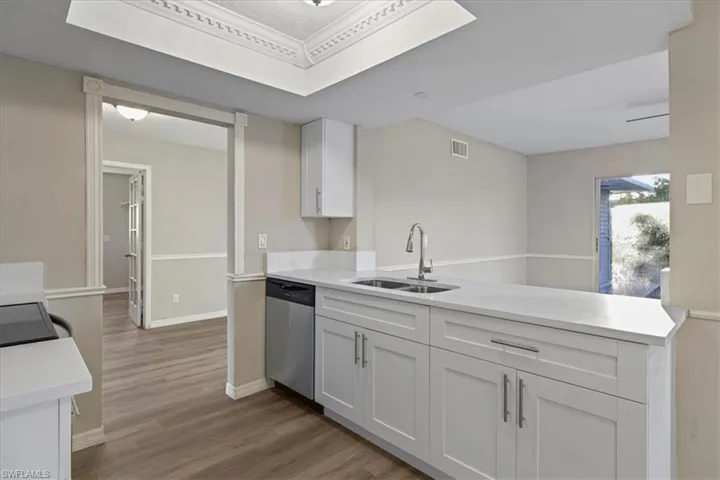 Kitchen with light wood-type flooring, a peninsula, stainless steel dishwasher, light stone countertops, and white cabinetry