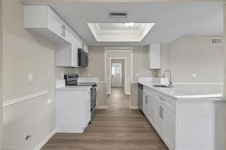 Kitchen with stainless steel appliances, white cabinets, dark wood-style flooring, a tray ceiling, and light stone countertops
