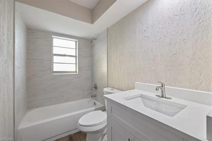 Full bathroom featuring a textured wall, vanity, tub / shower combination, and wood finished floors