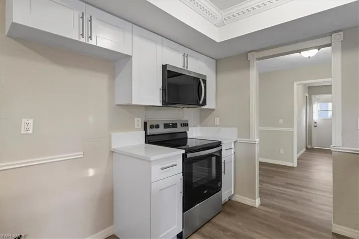 Kitchen featuring appliances with stainless steel finishes, white cabinetry, light wood-style flooring, and light stone countertops