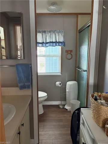 Bathroom featuring a shower with door, vanity, wood-type flooring, and toilet