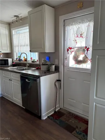 Kitchen with dark hardwood / wood-style flooring, white cabinetry, sink, and stainless steel dishwasher