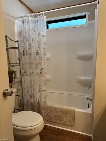 Bathroom with wood-type flooring, toilet, and shower / bath combination with curtain