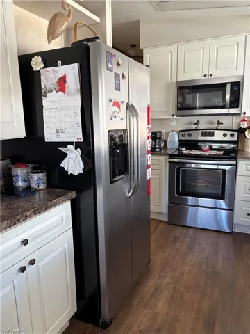 Kitchen featuring a textured ceiling, stainless steel appliances, vaulted ceiling, white cabinets, and dark hardwood / wood-style floors