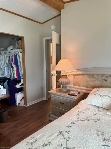 Bedroom with dark hardwood / wood-style floors, crown molding, and a closet