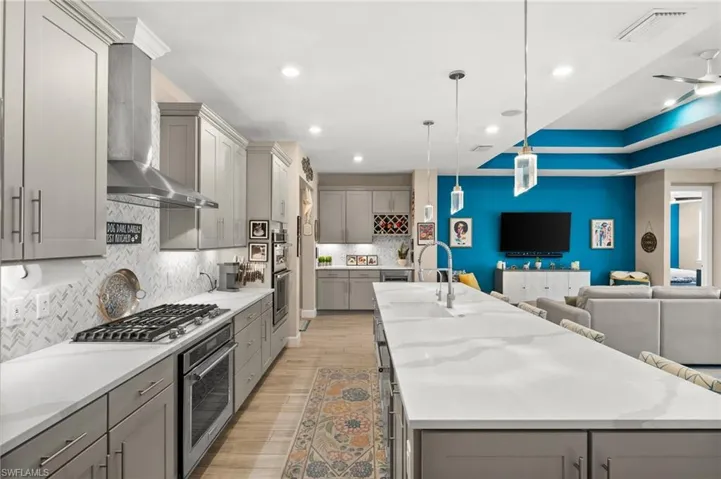 Kitchen featuring gray cabinets, stainless steel appliances, wall chimney range hood, open floor plan, and recessed lighting