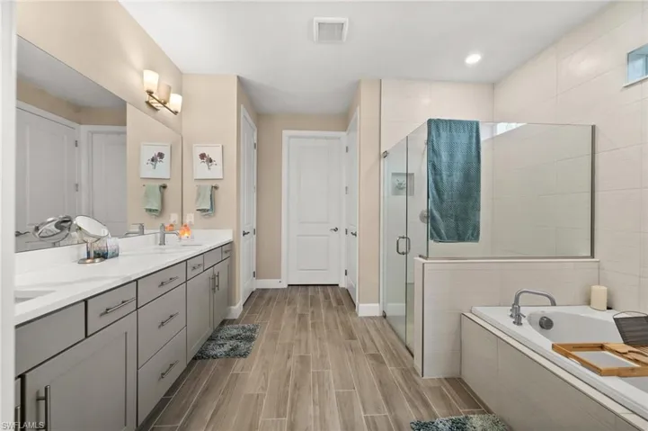 Full bathroom with a bath, a stall shower, double vanity, and wood finish floors