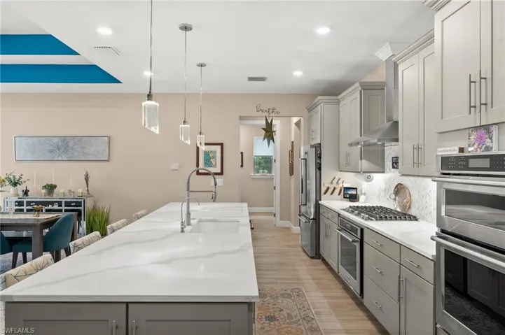Kitchen featuring stainless steel appliances, gray cabinets, an island with sink, tasteful backsplash, and recessed lighting