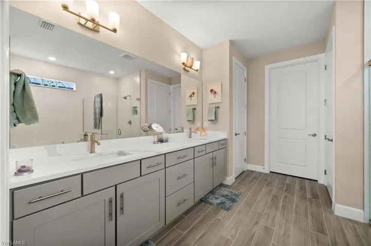 Full bathroom featuring double vanity, a shower stall, and wood-look tile floors