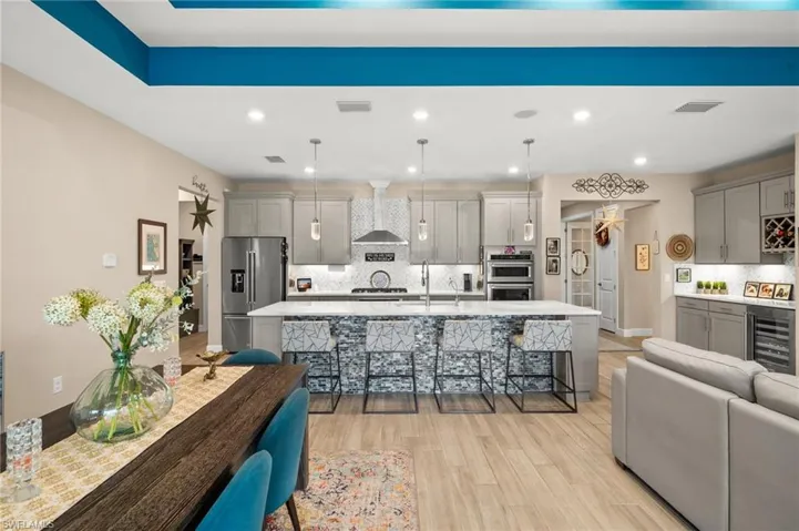 Kitchen featuring wine cooler, appliances with stainless steel finishes, gray cabinetry, wall chimney exhaust hood, and recessed lighting