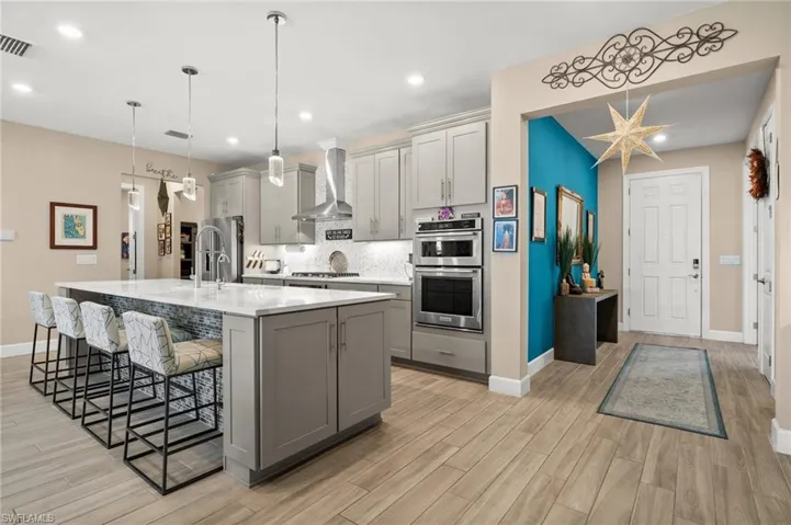 Kitchen featuring wall chimney range hood, gray cabinetry, stainless steel appliances, a breakfast bar, and recessed lighting