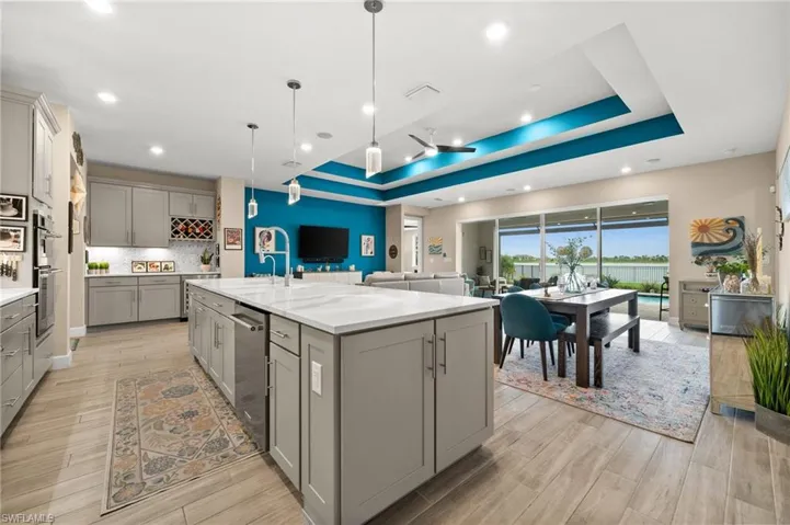 Kitchen with gray cabinetry, a raised ceiling, light wood-look tile flooring, a center island with sink, and tasteful backsplash