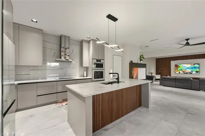 Kitchen with modern cabinets, gray cabinetry, decorative light fixtures, and wall chimney exhaust hood