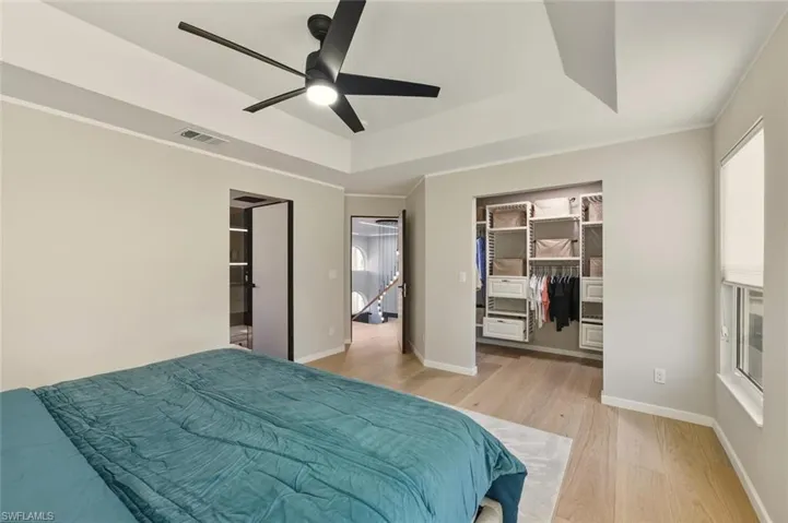 Bedroom featuring a spacious closet, light wood finished floors, a raised ceiling, ceiling fan, and crown molding