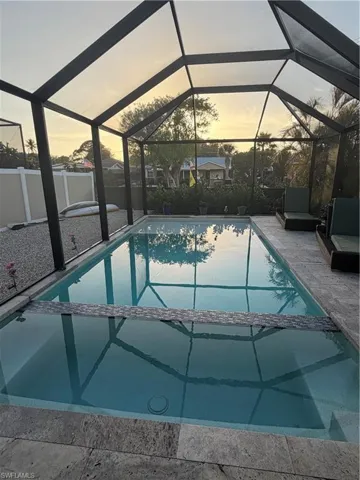 Pool at dusk with a pool with connected hot tub, a sunroom, a lanai, and a patio