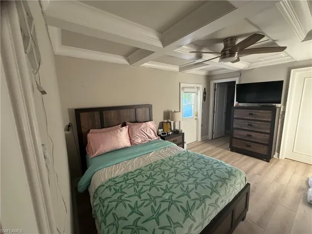 Bedroom featuring coffered ceiling, ornamental molding, light wood-style floors, and a ceiling fan
