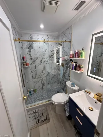 Bathroom with ornamental molding, vanity, and a marble finish shower
