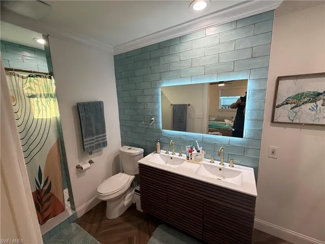 Bathroom featuring ornamental molding, double vanity, tile walls, a shower with shower curtain, and decorative backsplash