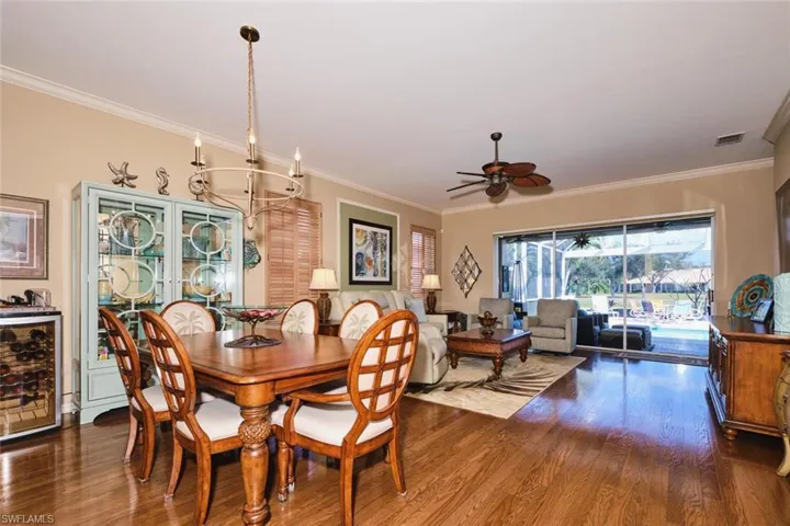Dining room featuring dark wood-type flooring, a ceiling fan, ornamental molding, hanging lights, and beverage cooler