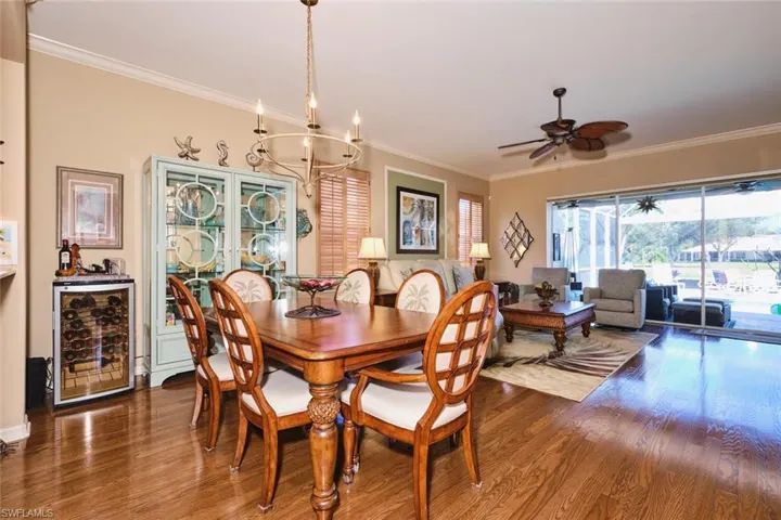 Dining area featuring wine cooler, crown molding, dark wood finished floors, a ceiling fan, and a chandelier