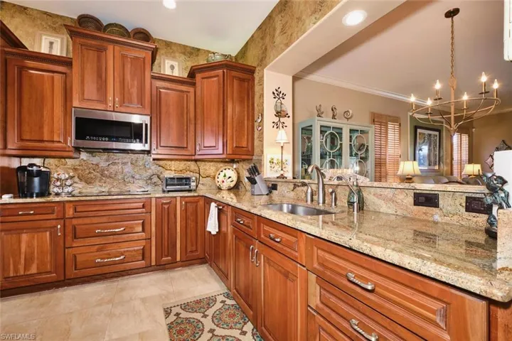 Kitchen with wood finish cabinets, light stone counters, stainless steel microwave, hanging lights, and decorative backsplash
