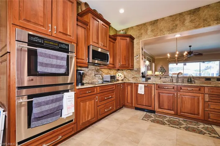 Kitchen featuring wood finish cabinetry, stainless steel appliances, suspended lighting, and light stone counters