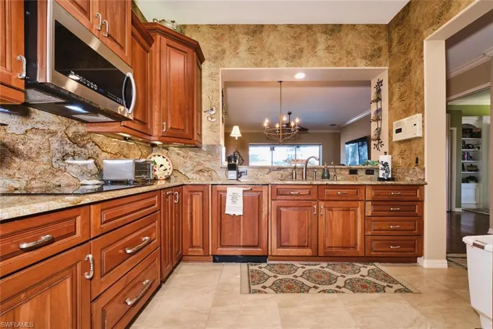 Kitchen with wood finish cabinetry, ornamental molding, stainless steel microwave, light stone counters, and suspended lighting